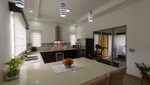 A modern kitchen with a central island, stainless steel appliances, pendant lighting, and a view of the living area through glass doors. - Arenal White Bliss Villa (La Fortuna)