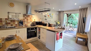 A modern kitchen with a built-in oven, microwave, and sink. There is a dining area with a wooden table and chairs. - Ty Barddu (Newcastle Emlyn)