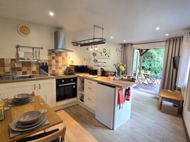 Una cocina moderna con horno empotrado, microondas y lavamanos. Hay una zona de comedor con una mesa y sillas de madera.