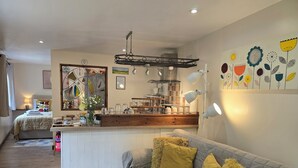 A cozy living room with a grey sofa and yellow cushions, a wooden coffee table, and a kitchen area with a wooden counter and hanging lights. - Ty Barddu (Newcastle Emlyn)
