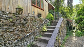 A stone staircase leading to a wooden house with a metal railing and potted plants. - Ty Barddu (Newcastle Emlyn)