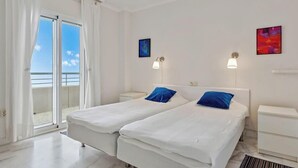 A hotel room with two beds, a balcony, and a view of the sea.