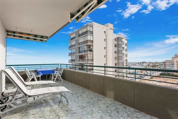 A balcony with a table and chairs, a view of a tall building, and a clear sky.