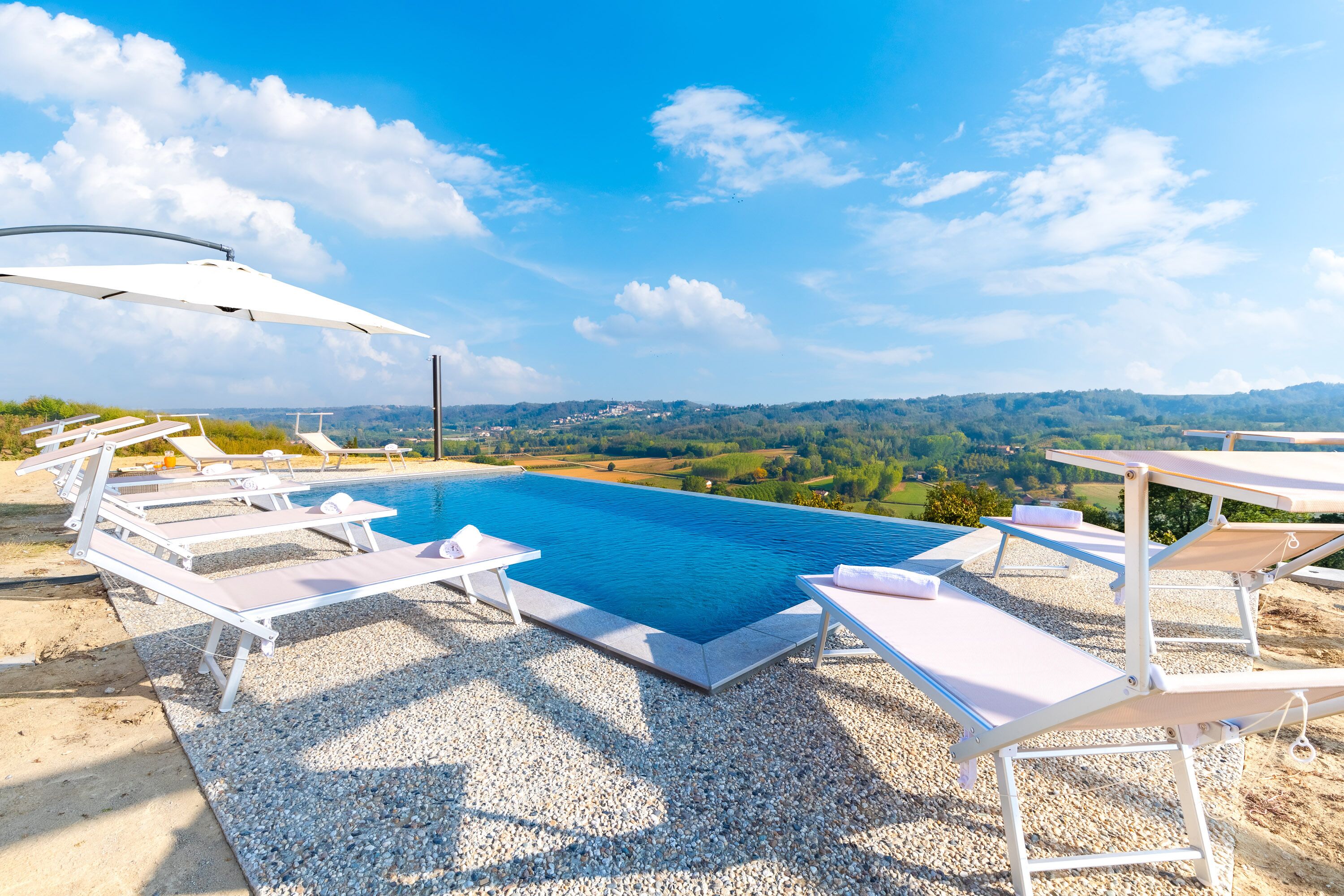 Ein Pool mit Liegestühlen und Sonnenschirmen, umgeben von Kieswegen und mit Blick auf eine schöne Landschaft.