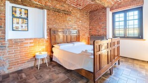 A bedroom with a brick wall, a wooden bed, a small bedside table, and a window with blinds. - Casa Leonarda 8+2, Emma Villas (Belveglio)
