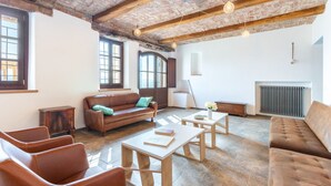 A spacious living room with a brown leather sofa, a wooden coffee table, and a brown leather armchair. There is a radiator on the wall and a window with a view of the outside. - Casa Leonarda 8+2, Emma Villas (Belveglio)