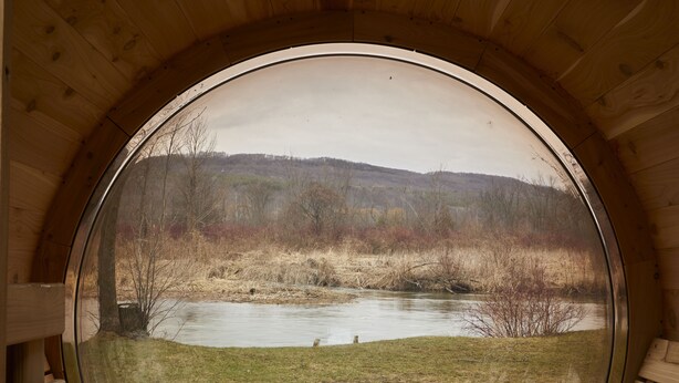 A wooden cabin with a circular window offering a view of a river and surrounding landscape. - The June Motel, Beaver Valley (Grey Highlands)