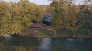 A lakeside cabin with a deck and outdoor seating area, surrounded by trees and a river. - The June Motel, Beaver Valley (Grey Highlands)