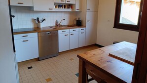 A compact kitchen with white cabinets, a dishwasher, and a wooden table. - LA Villa DES Tacounets (Saint-Gervais-les-Bains)