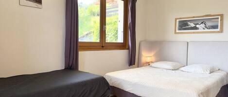A bedroom with two beds, a window with curtains, a mounted picture, and a lamp.