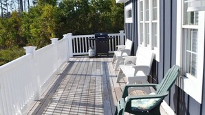Une terrasse en bois avec des rampes blanches, un barbecue et des sièges d’extérieur.