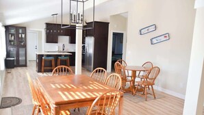 Un grand espace à manger avec une table et des chaises en bois, une cuisine en arrière-plan et un tapis à motifs sur le sol.