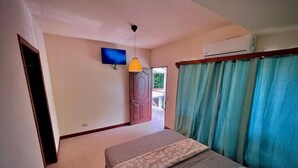 Una camera da letto con un letto, una televisione, un ventilatore a soffitto e una finestra con tende.