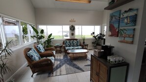Ein geräumiges Wohnzimmer mit Rattanmöbeln, einem großen Fenster und Blick ins Freie.
