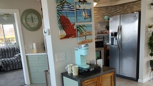 Eine moderne Küche mit integriertem Kühlschrank, einer Kaffeemaschine und einem kleinen Schrank. An der Wand befinden sich dekorative Wandbilder und eine Uhr.