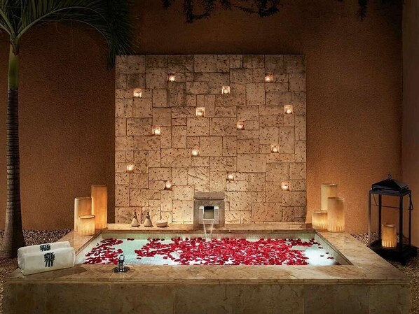 A spa area with a stone wall, candles, and a pool with rose petals.