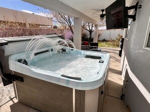 A hot tub with water jets, attached to a covered patio area with a ceiling fan and a mounted TV. - Gorgeous house w/hot tub pool table gaming table next to amazing walking trail! (Albuquerque)