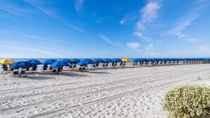 Una playa con hileras de sillas y sombrillas, arena y un cielo despejado.