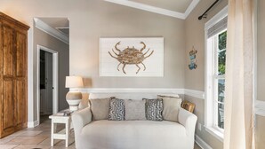 Una sala de estar con un sofá blanco, cojines estampados, una obra de arte colgada en la pared, una lámpara y un mueble de madera.