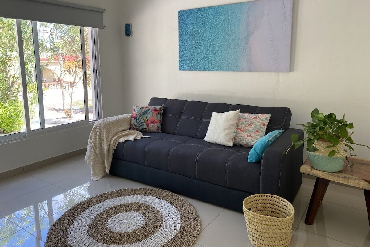 Un salon avec un canapé foncé, un tapis à motifs, une plante en pot et un tableau accroché au mur.