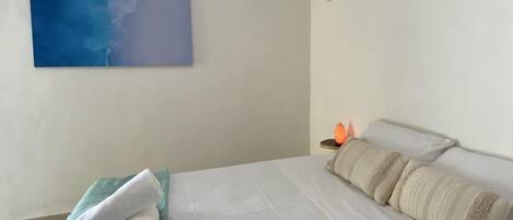 A hotel room with a bed, a blue towel, a white pillow, and an air conditioning unit.
