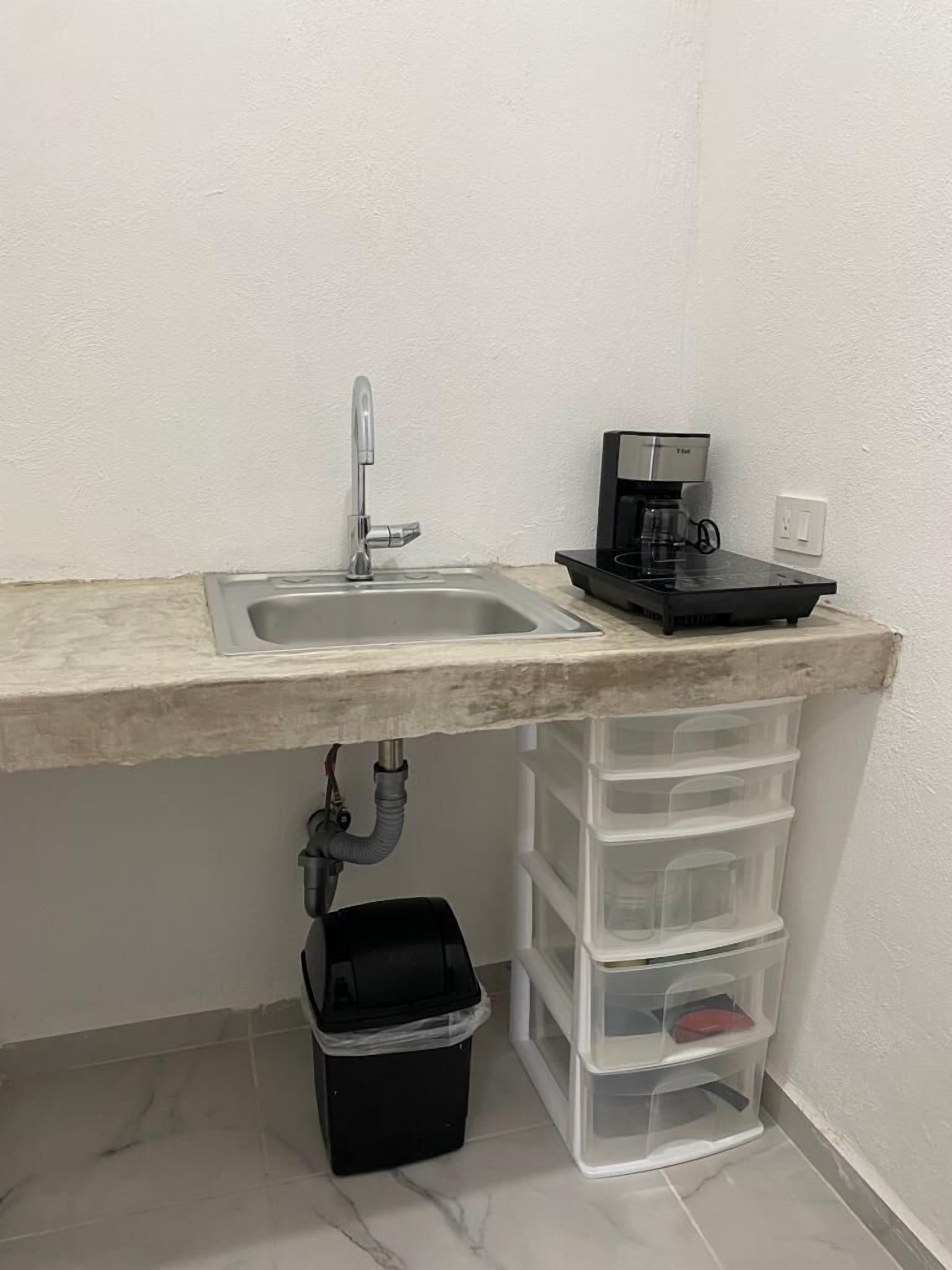 A small kitchen area with a sink, a coffee maker, and storage drawers.
