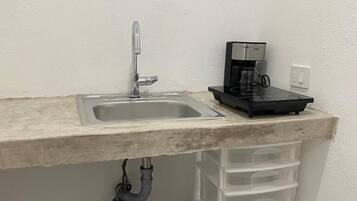 A small kitchen area with a sink, a coffee maker, and storage drawers.