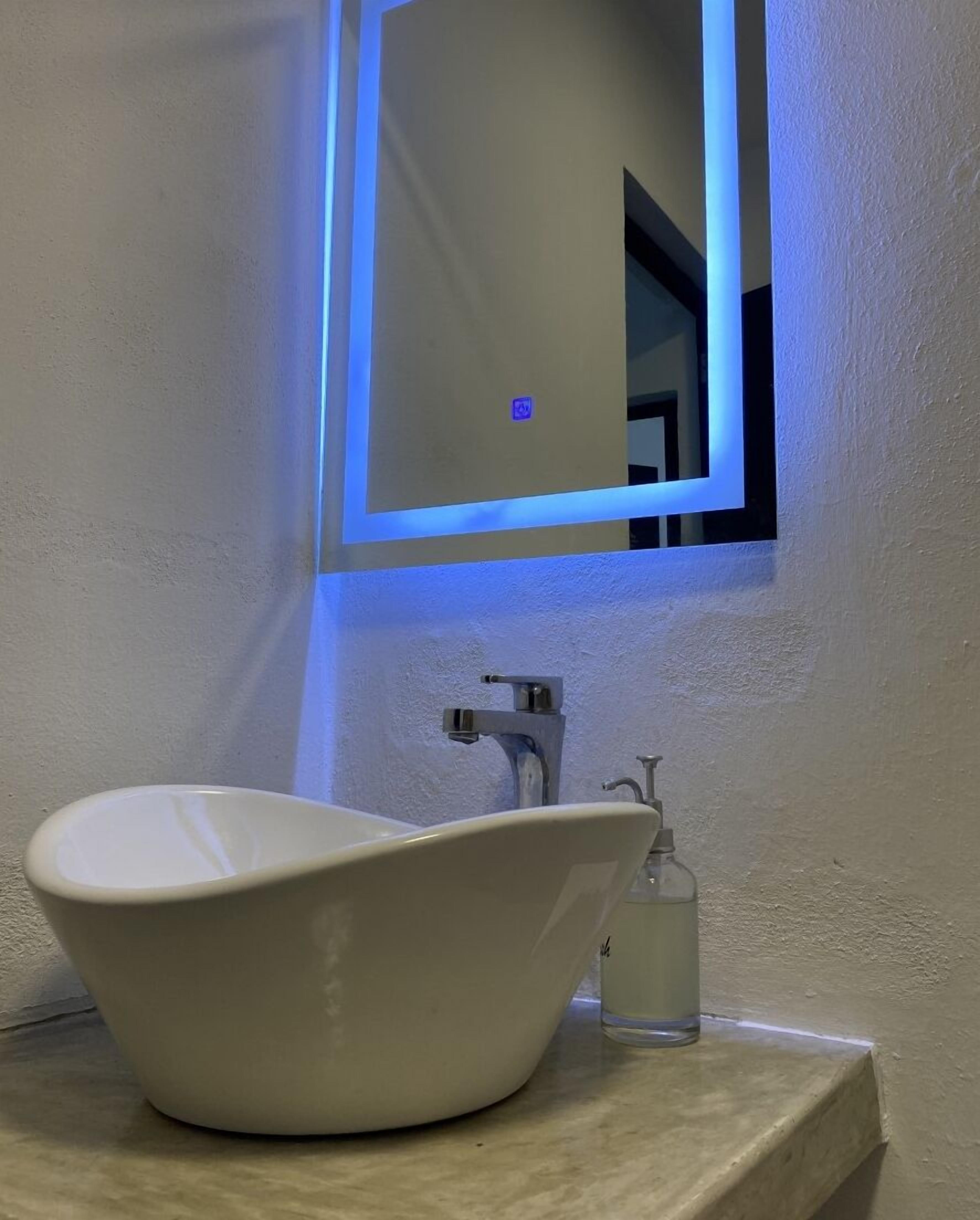 A bathroom with a white vessel sink, a mirror with a blue light, and a small bottle of hand sanitizer on the counter.