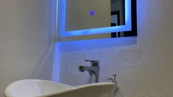 A bathroom with a white vessel sink, a mirror with a blue light, and a small bottle of hand sanitizer on the counter.