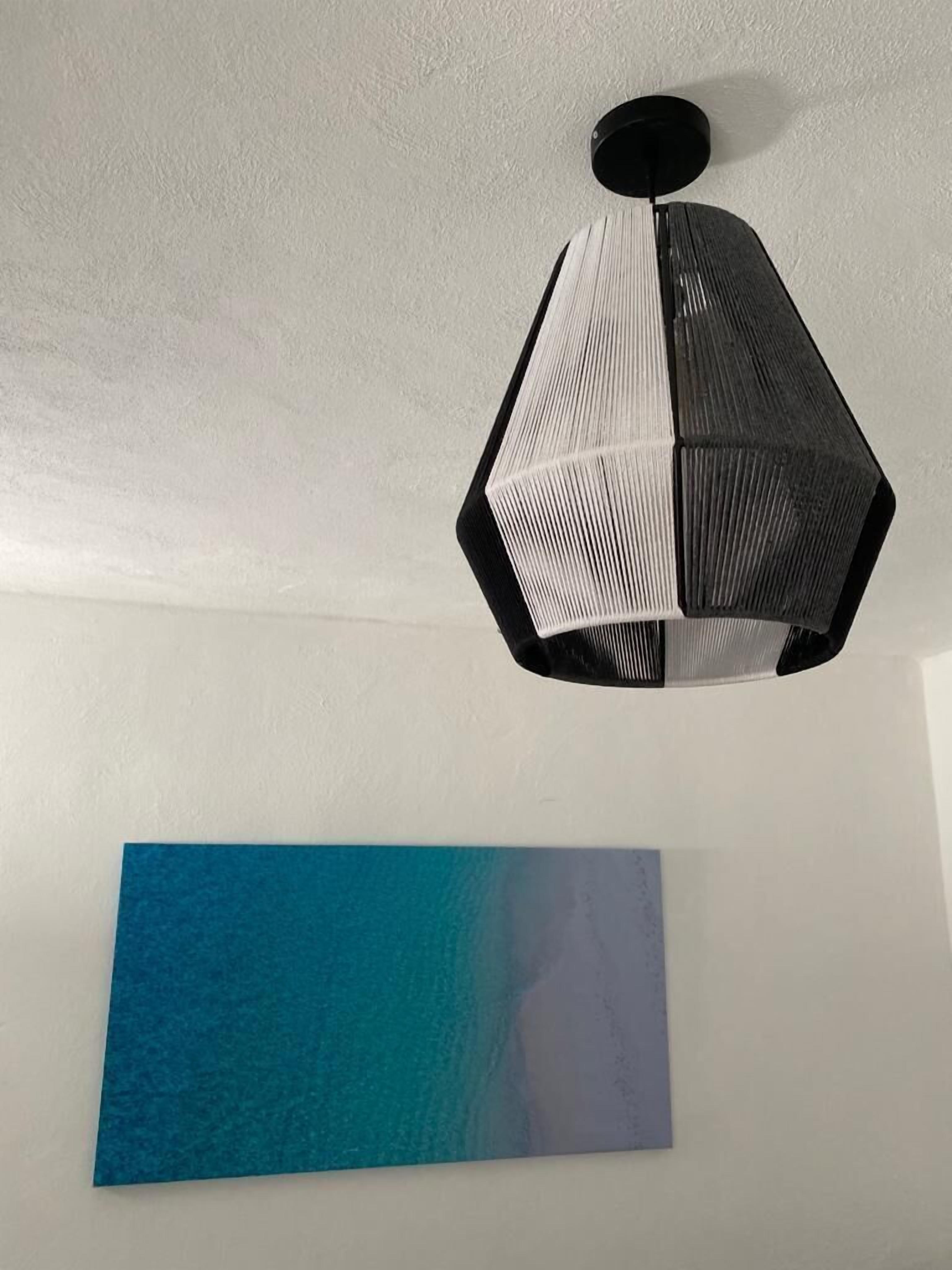 Una habitación con una lámpara colgante de diseño geométrico en negro y una obra de arte mural con degradado azul.