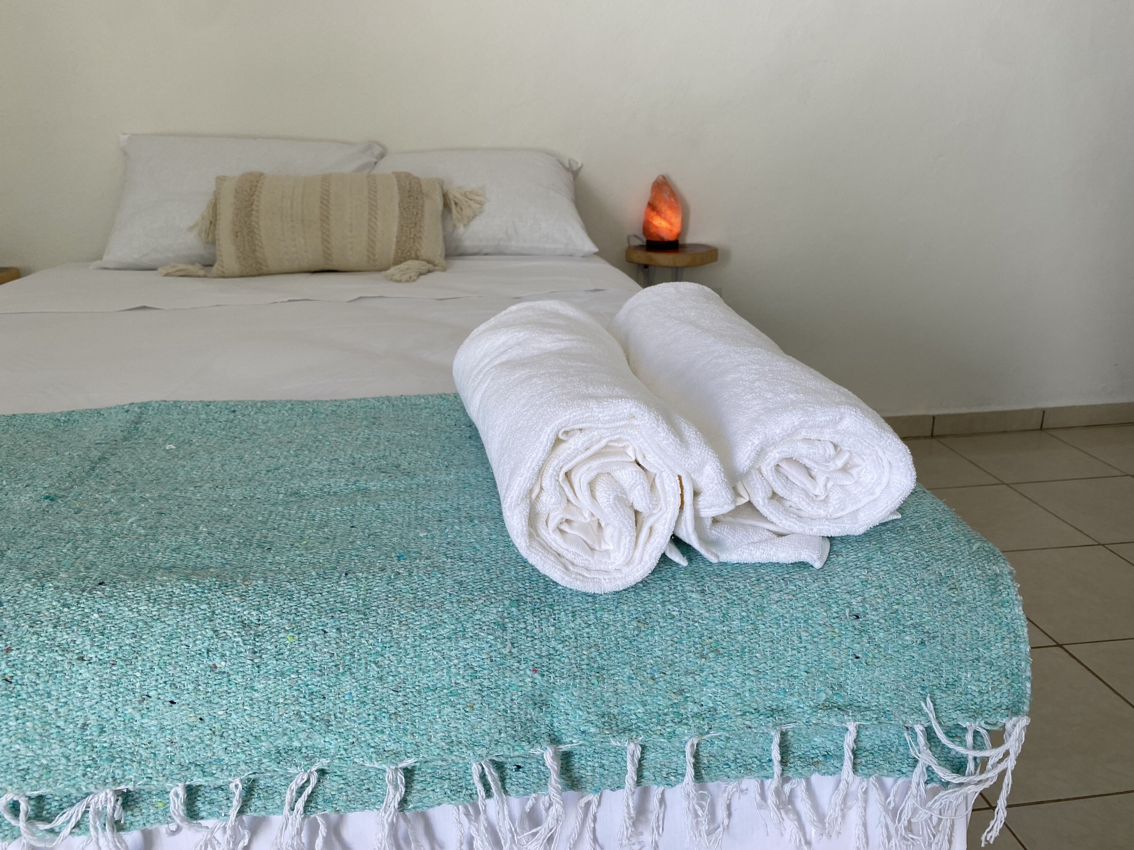 A bed with white linens, a teal throw blanket, and rolled white towels.