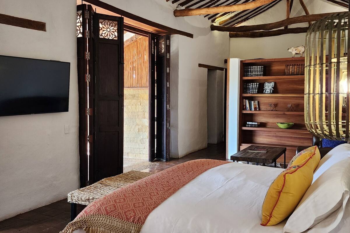 A bedroom with a bed, a television, a bookshelf, and a decorative hanging light fixture.