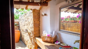 Un baño con pared de piedra, un banco de madera, una cesta de mimbre con toallas y un cuenco decorativo.