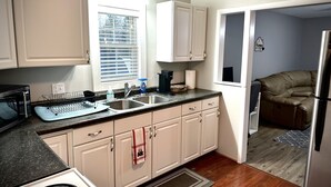 Una cocina con armarios blancos, encimera negra y ventana con persianas.