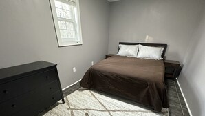 Un dormitorio con cama, cómoda, mesitas de noche y ventana.