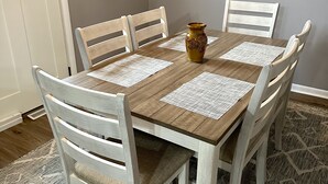 Una mesa de comedor con seis sillas blancas, un florero y manteles individuales.