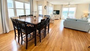 A spacious living area with a wooden dining table and chairs, a light blue sofa, and a television. - BEACH PLEASE! Amazing Ocean and Sound Views with Easy Beach Access! Pet Friendly (North Topsail Beach)
