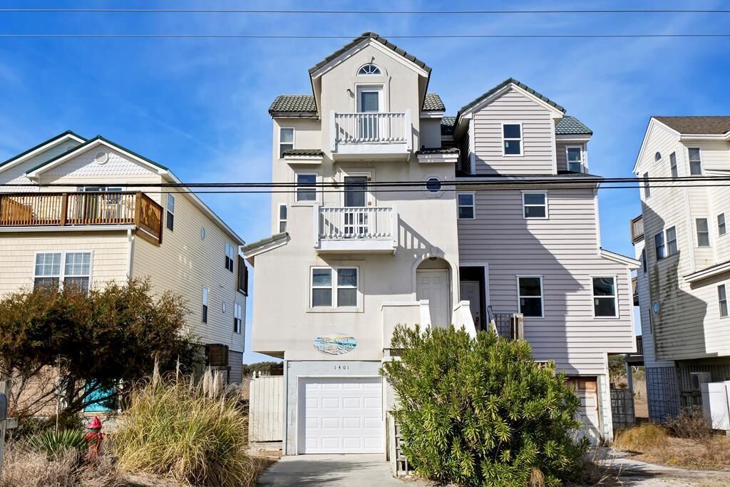 A multi-story residential building with a garage, a balcony on the second floor, and a small porch.