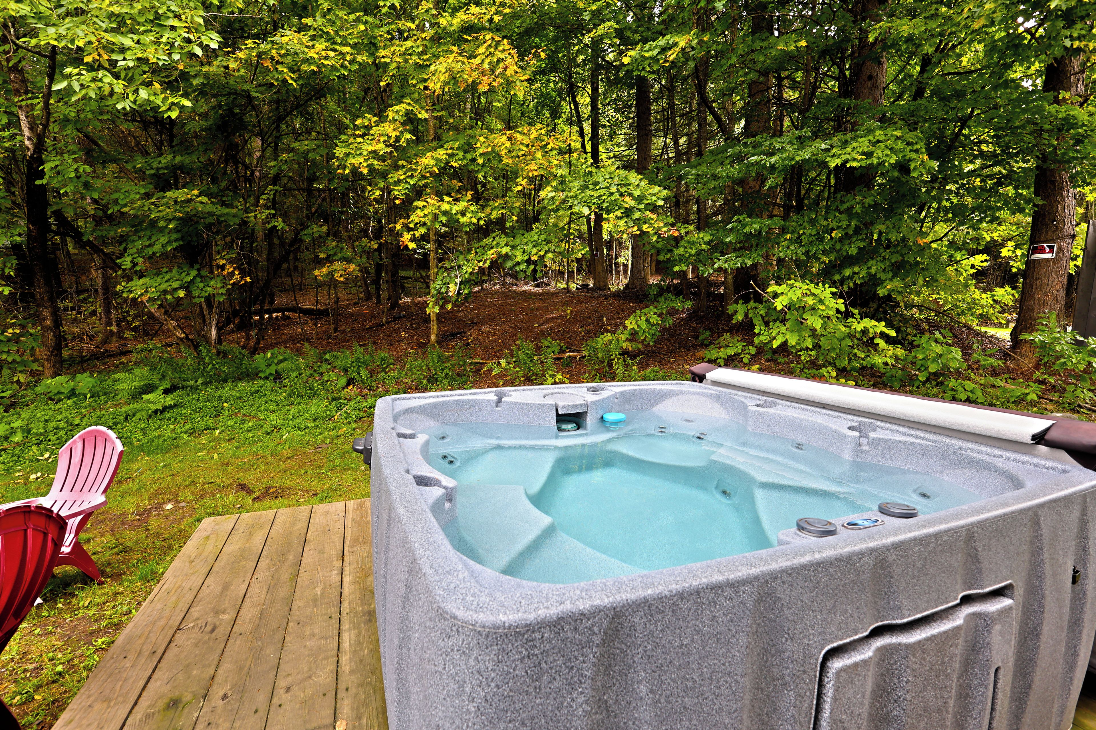 A hot tub in a wooded area with a wooden deck and a red chair.
