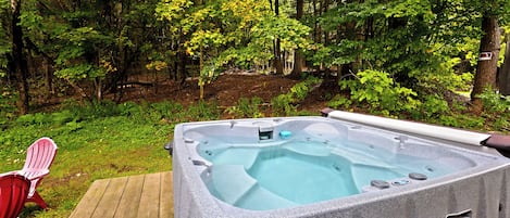 A hot tub in a wooded area with a wooden deck and a red chair.