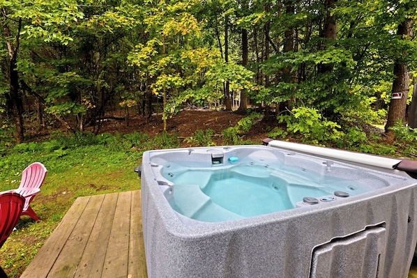 A hot tub in a wooded area with a wooden deck and a red chair.