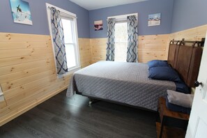 Un dormitorio con cama, paredes de paneles de madera, una ventana con cortinas y obras de arte en las paredes.