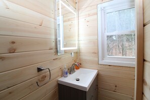 Un baño rústico con cabaña, que incluye un lavamanos blanco, un espejo y un ventanal.