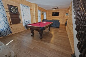 A room with a pool table, a dartboard, a television, and a ceiling fan.