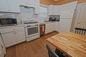 Una cocina con armarios blancos, microondas, estufa, horno y una mesa de comedor de madera.