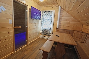 A wooden interior with a television mounted on the wall, a door with a glass panel, and a bench.