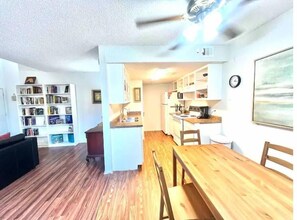 Un espacio habitable compacto con suelo de madera, una zona de comedor con mesa y sillas, una kitchenette y una estantería.