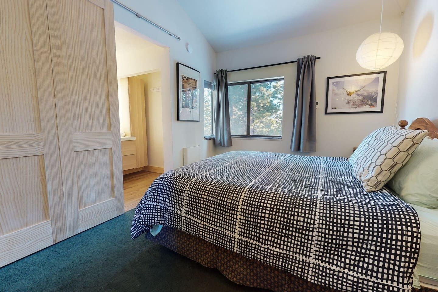 Ein Schlafzimmer mit einem großen Bett, einem Kleiderschrank, einem Fenster mit Vorhängen und einer Pendelleuchte.