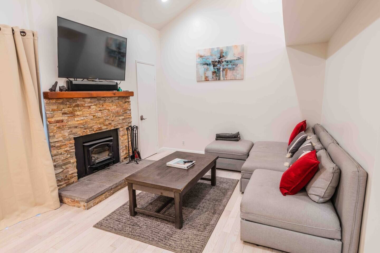 A living room with a stone fireplace, a flat-screen TV, a grey sofa with red cushions, and a coffee table.