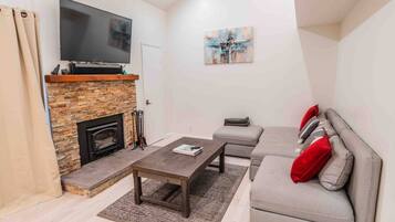A living room with a stone fireplace, a flat-screen TV, a grey sofa with red cushions, and a coffee table.